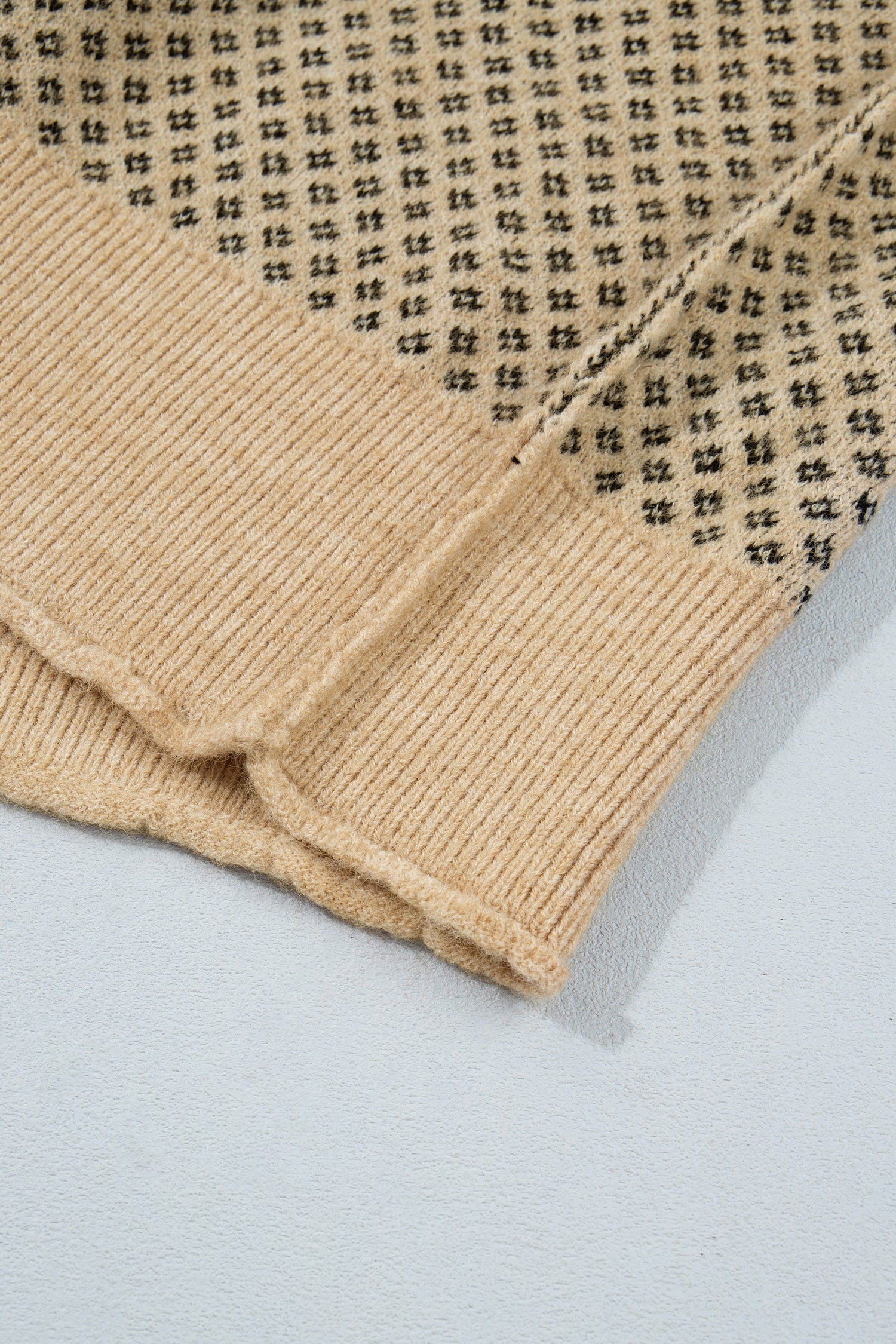 Close-up of a beige knit garment with black printed text pattern, showing folded fabric and ribbed texture on a light gray background.