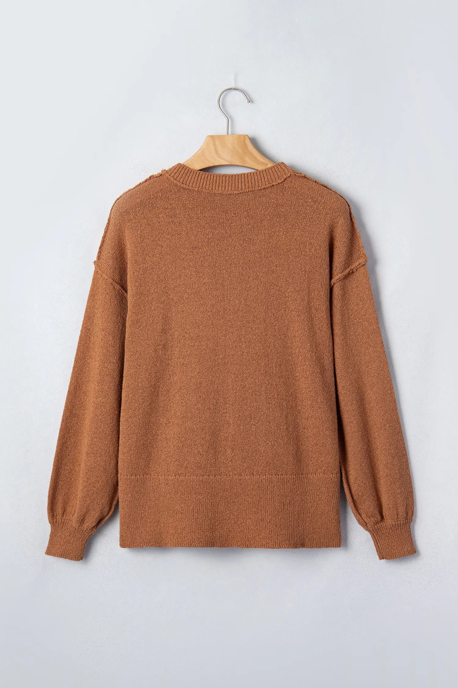 A rust-brown knit sweater with balloon sleeves, hanging on a wooden hanger against a light gray background.