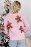 Back view of woman in light pink knit sweater with brown gingerbread motifs, red bows, and blue jeans.