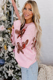Woman in light pink knit sweater with brown gingerbread pattern standing by decorated Christmas tree.