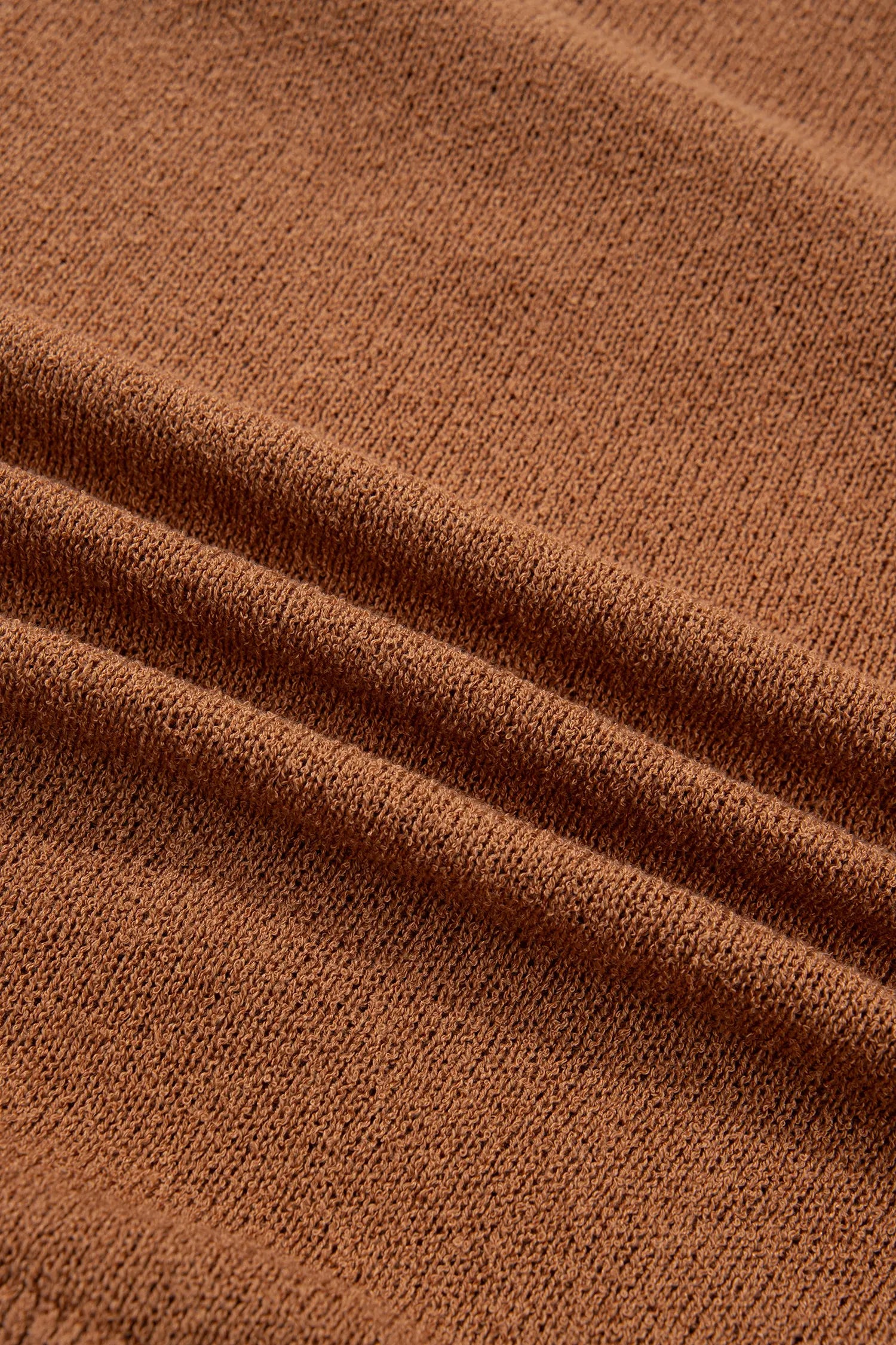 A close-up of a rust-brown knit fabric with soft folds showing the fine woven texture.