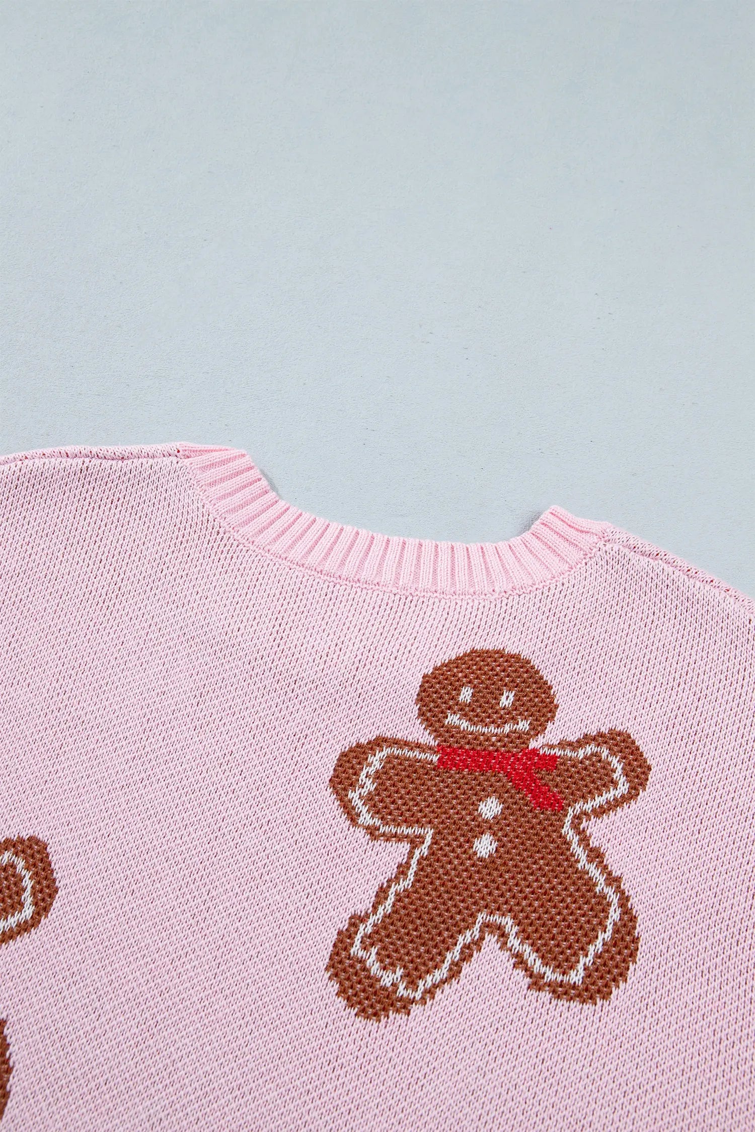 Close-up of light pink knit sweater with brown gingerbread man motif and red bow tie against blue-gray.