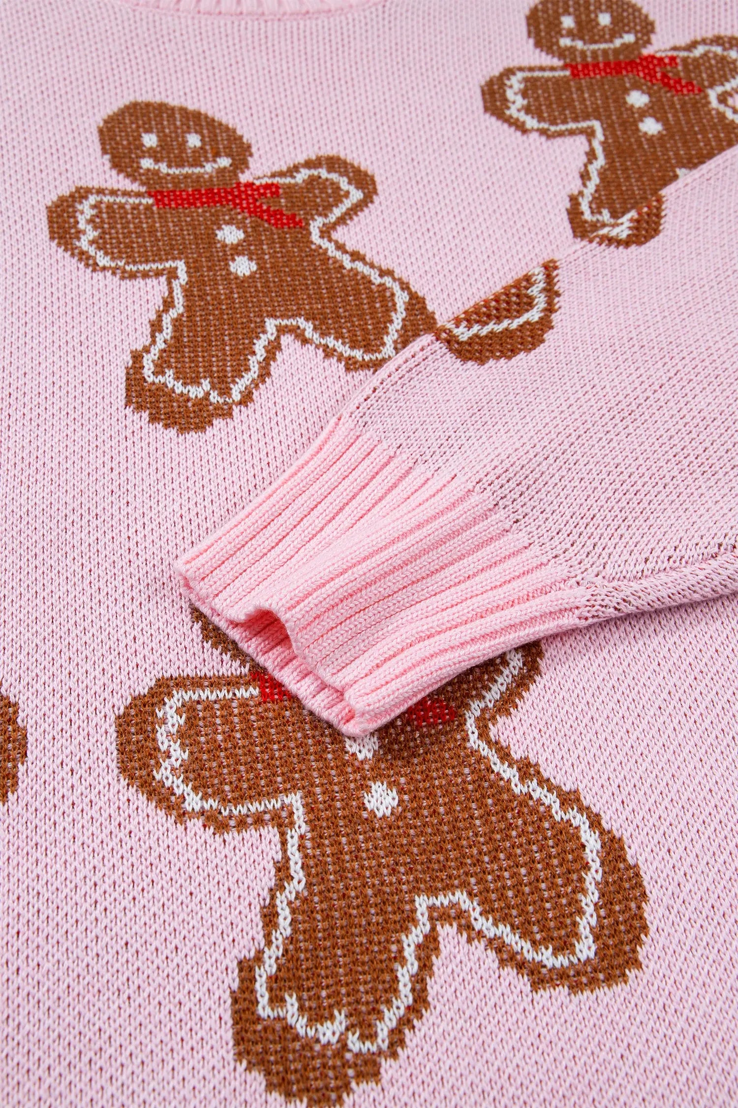 Close-up of pink knit sweater with brown gingerbread motifs, white outlines, and red accents.