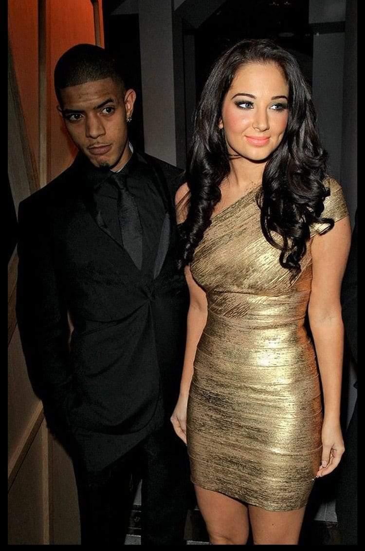 Man in a black suit and woman in a gold dress standing together indoors.