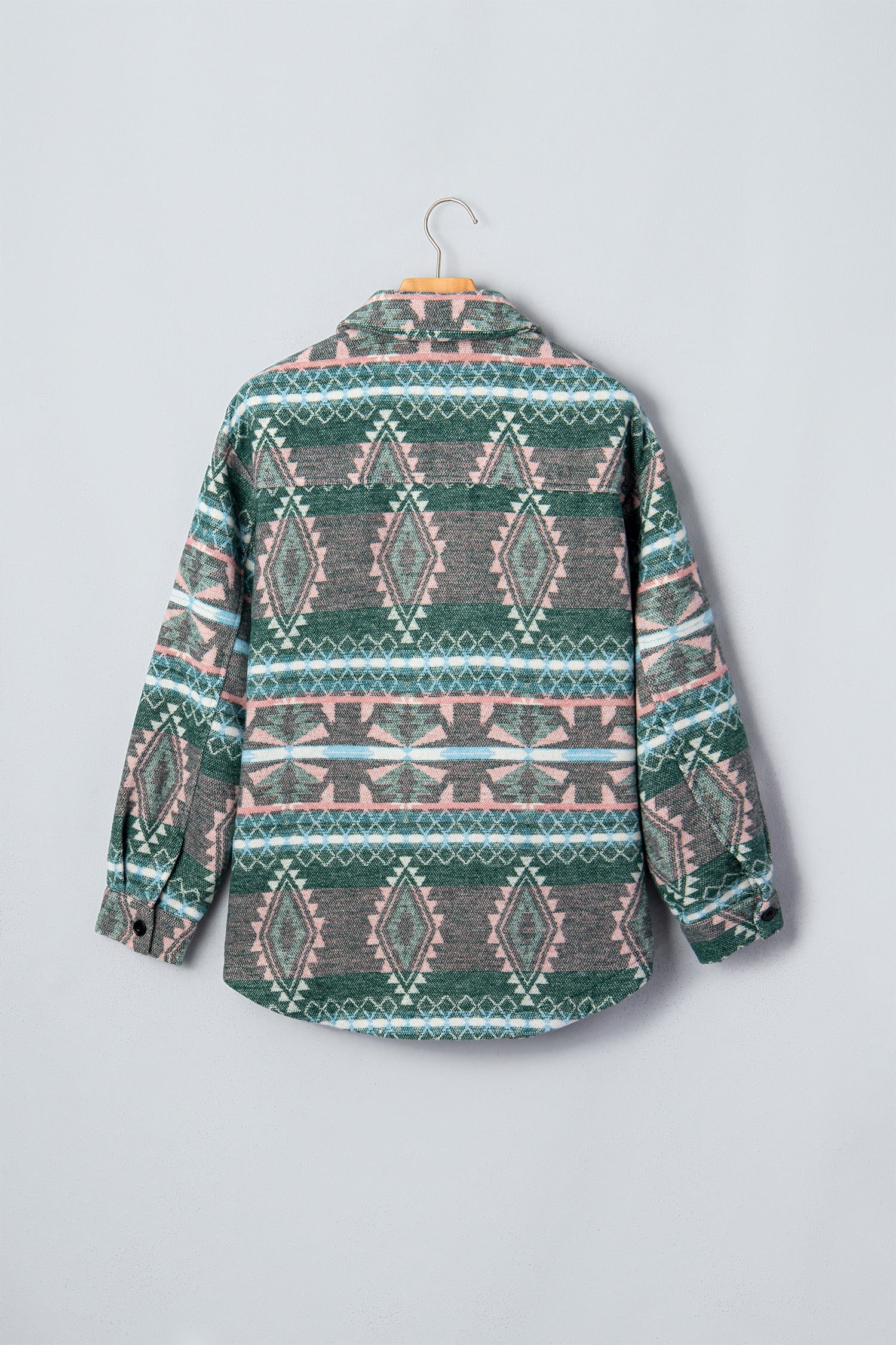 A long-sleeve button-up shirt with a green, pink, and gray geometric pattern, hanging on a wooden hanger against a light gray background.