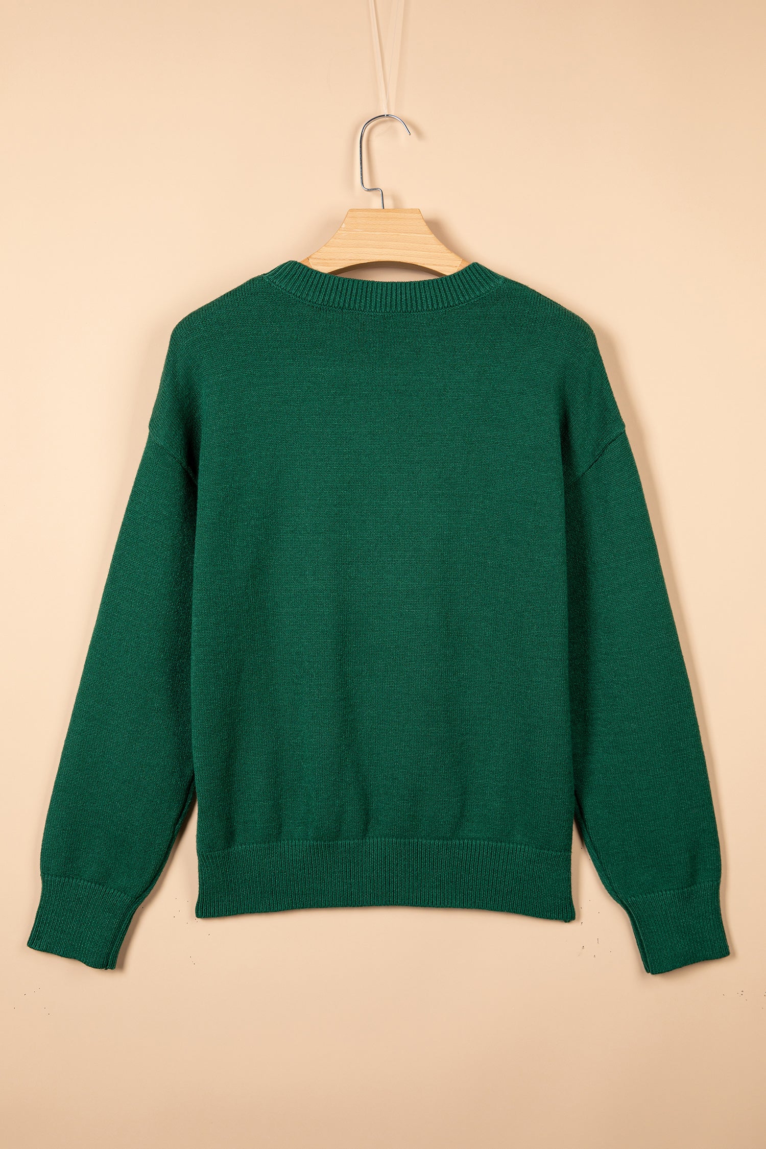 A dark green knit sweater hanging on a wooden hanger against a solid beige background.