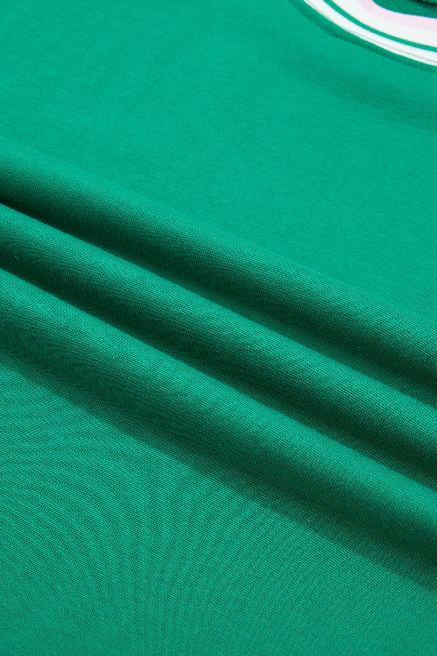 A close-up of bright green fabric with soft diagonal folds and a small portion 