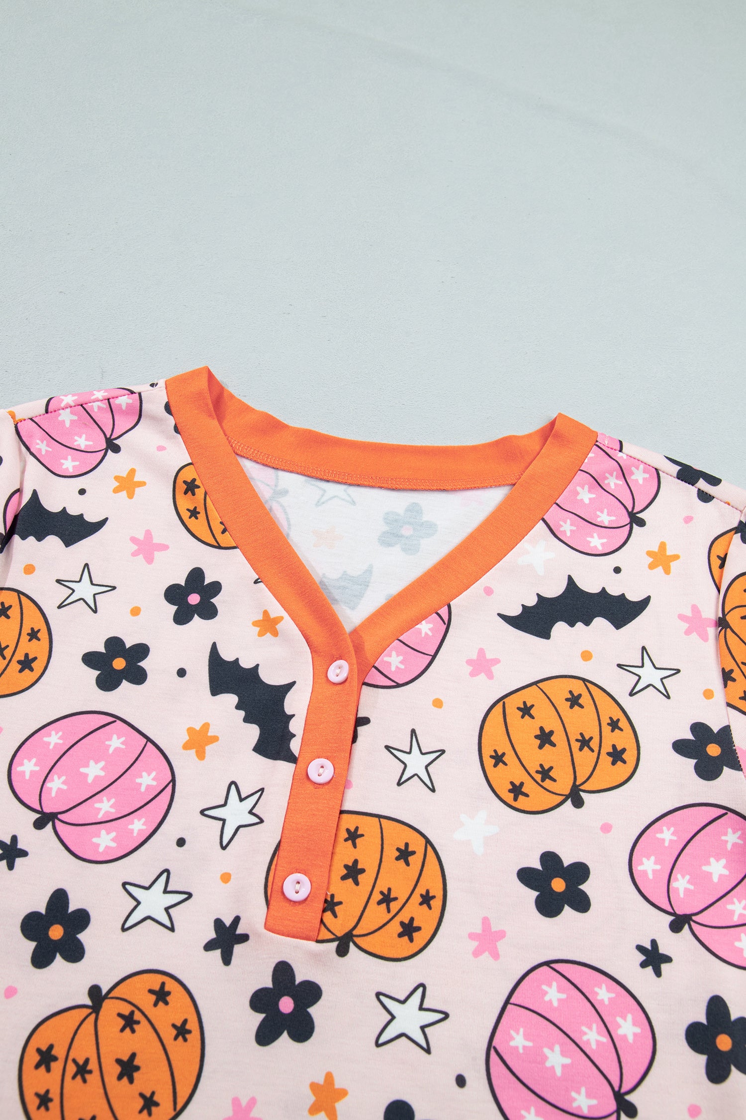 Close-up of pink Halloween top with pumpkins, bats, stars, and orange Henley collar.