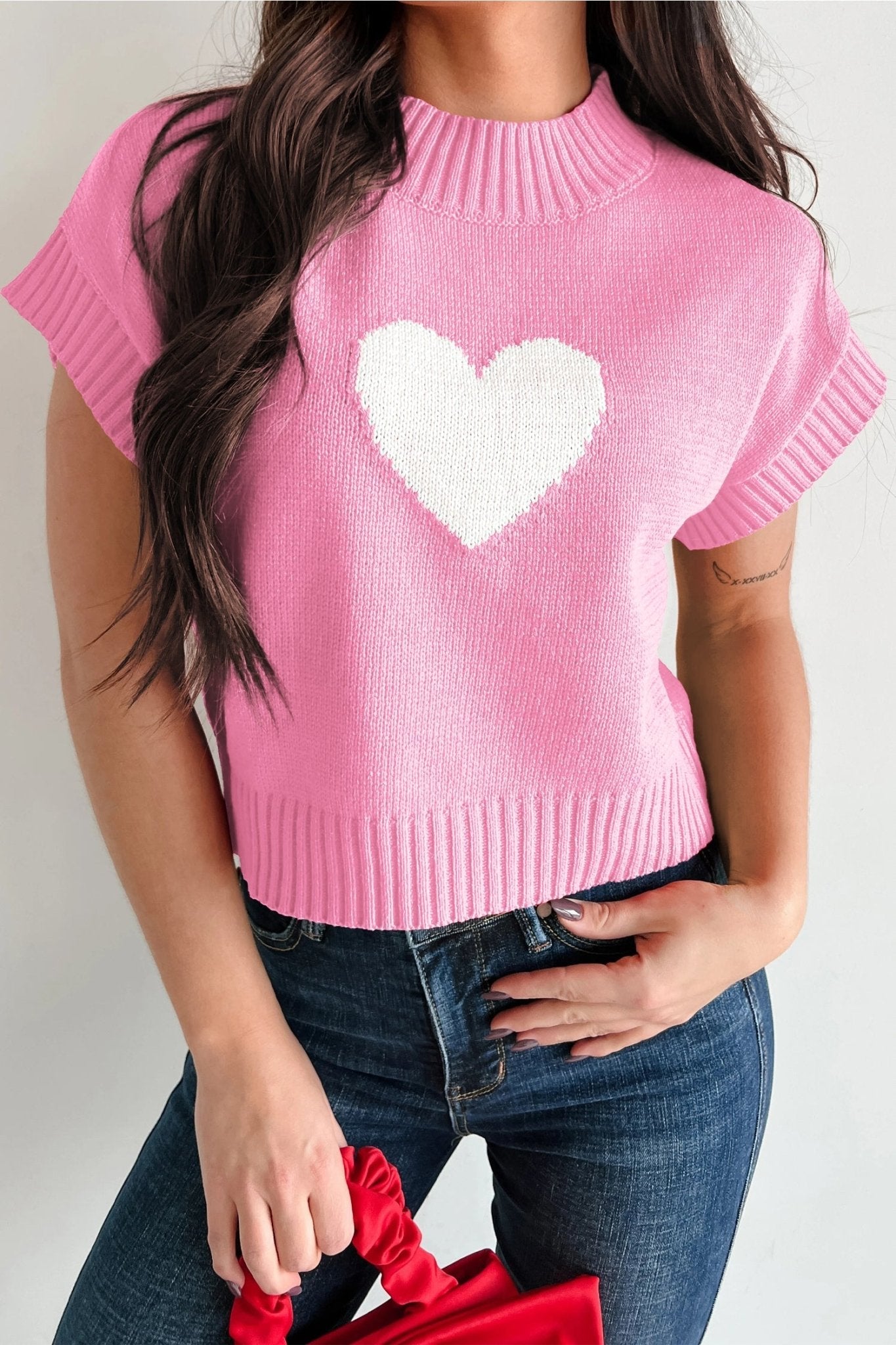 Person wearing a pink sweater with a white heart design on a plain background
