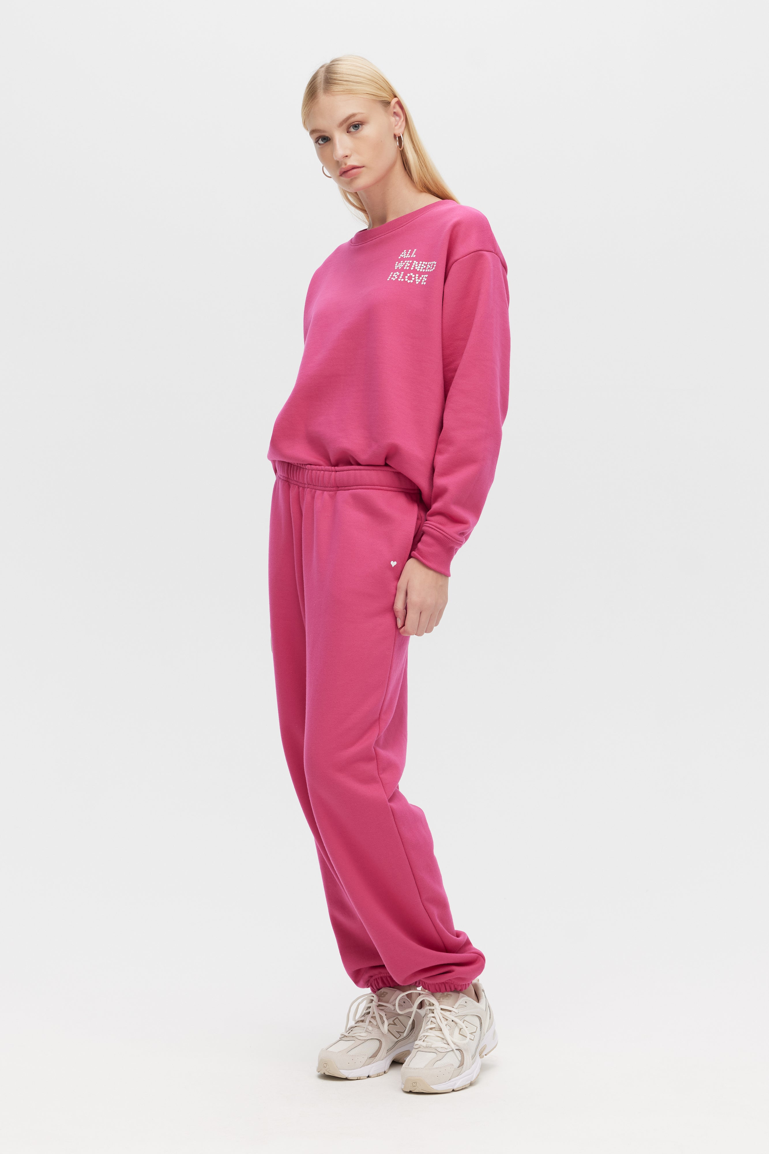 Person wearing a pink tracksuit with a white logo on a white background