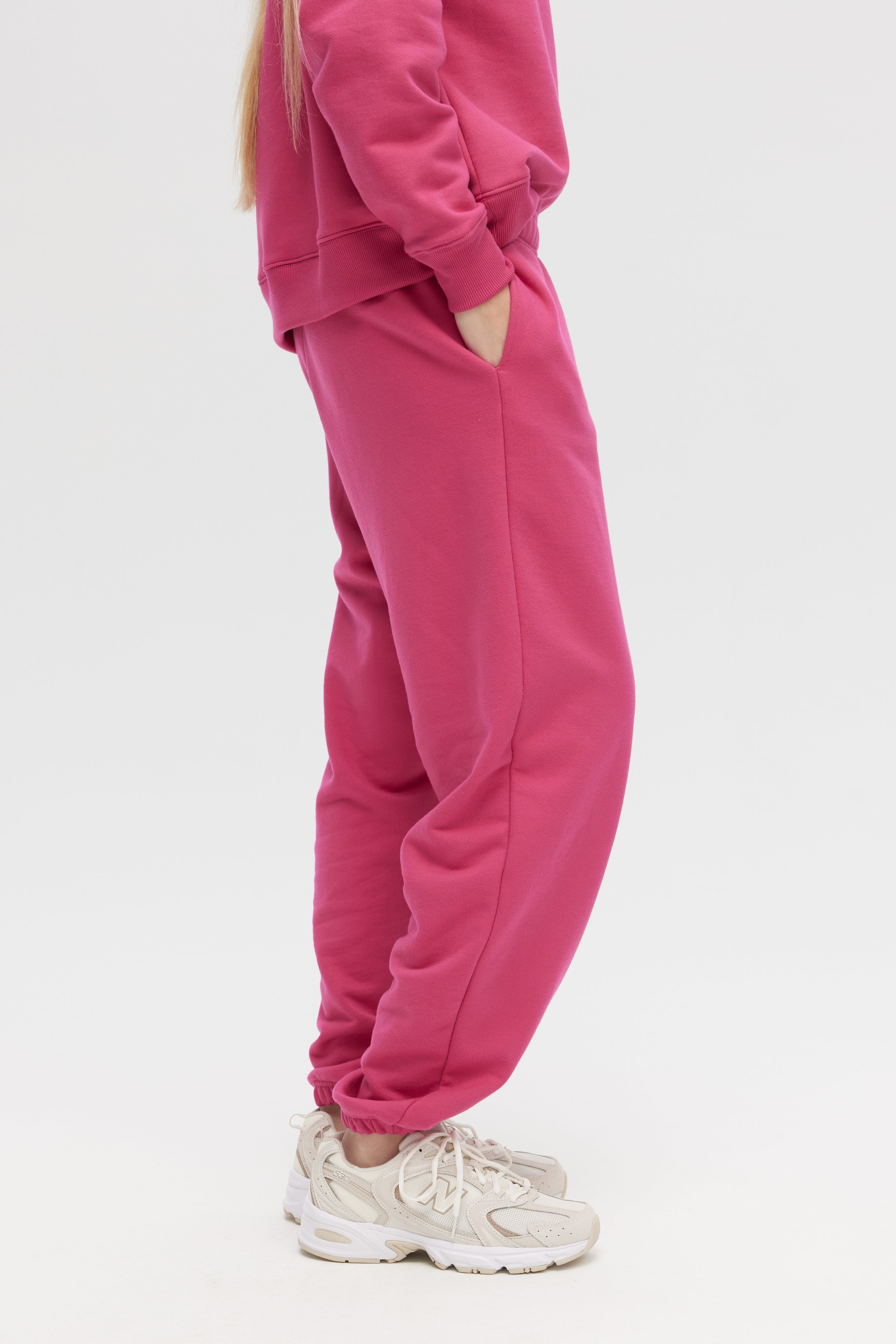 Person wearing a pink tracksuit with white sneakers on a light gray background