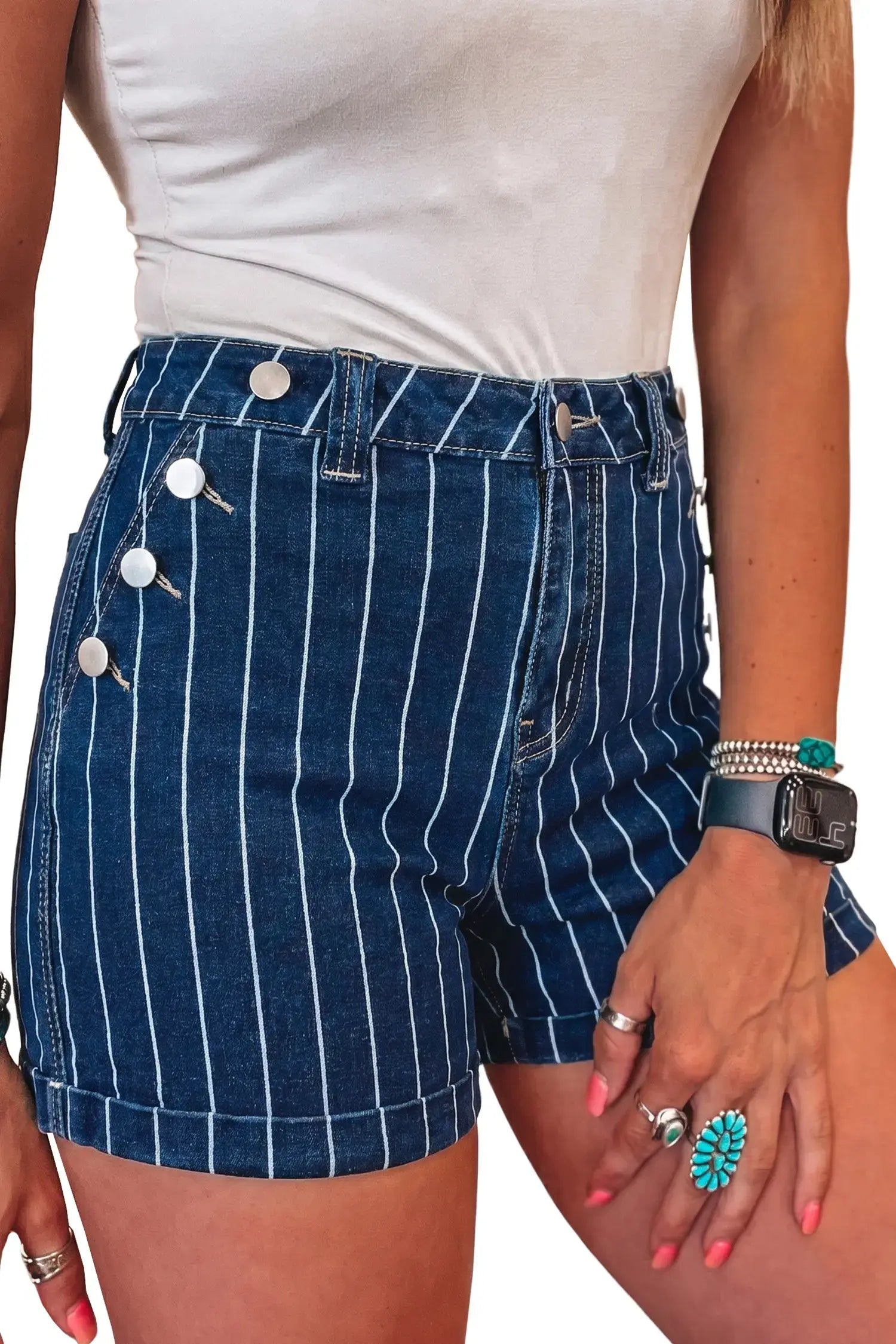 A close-up of a person wearing dark blue denim shorts with thin white vertical pinstripes and decorative silver-tone buttons on the side, paired with a white top against a plain white background.