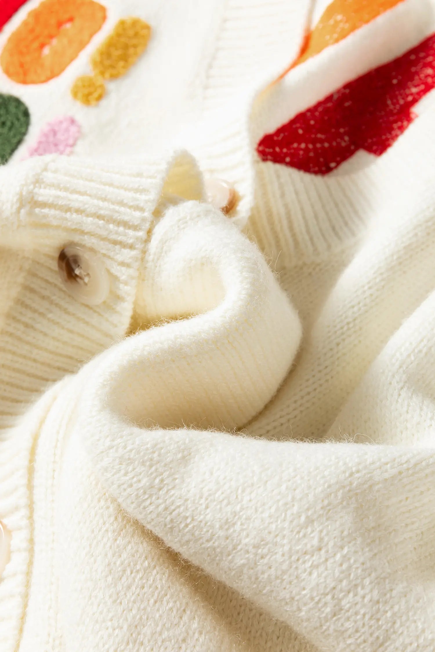 Close-up of a cream-colored knit sweater with colorful embroidered details and a ribbed buttoned collar.