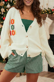 A woman wearing a cream knit cardigan with colorful 'COOL' lettering on the front, styled over a green top and green-and-white gingham shorts in a holiday home setting.