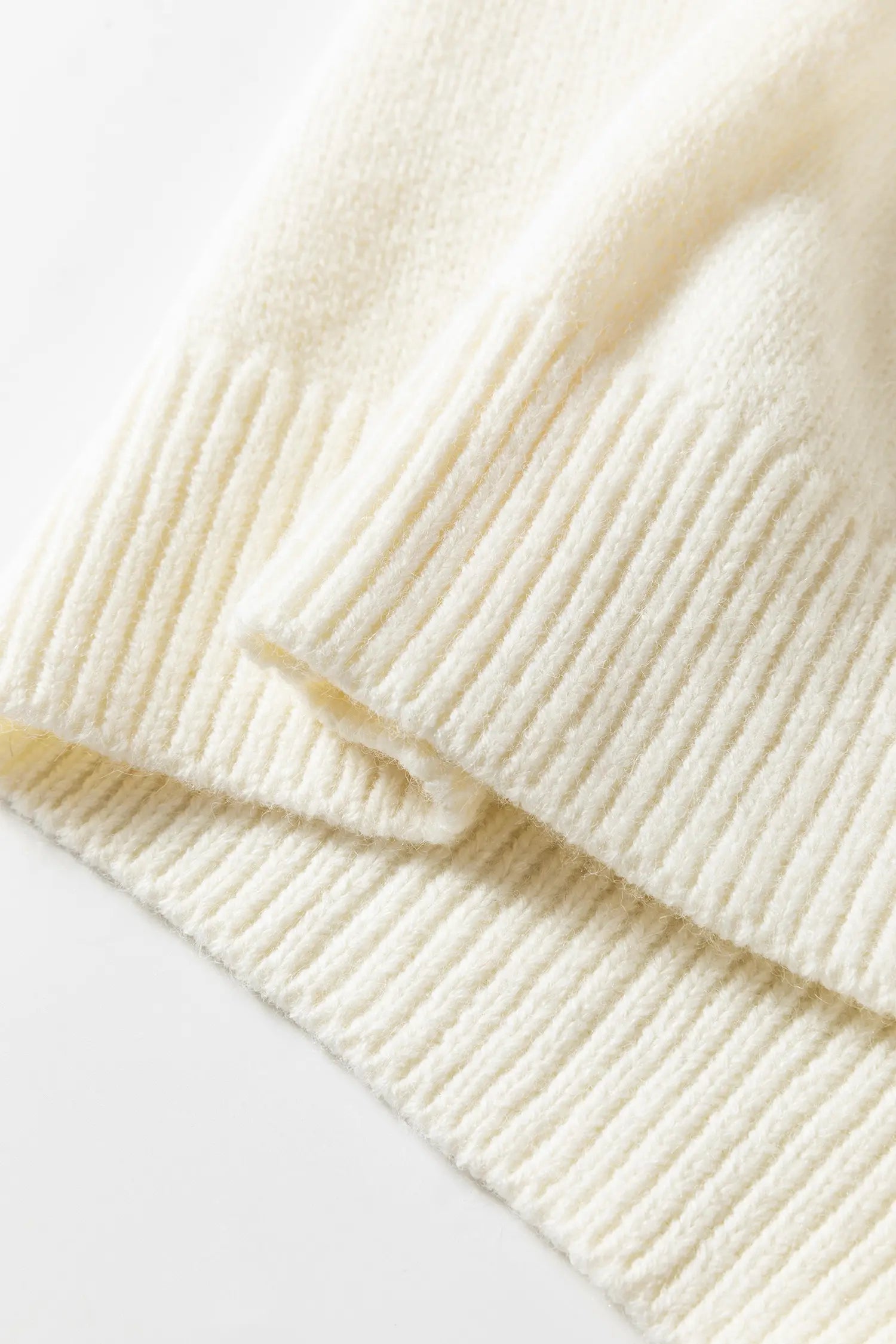Close-up of a cream-colored ribbed knit fabric, showing the soft texture and folded layers of the material.