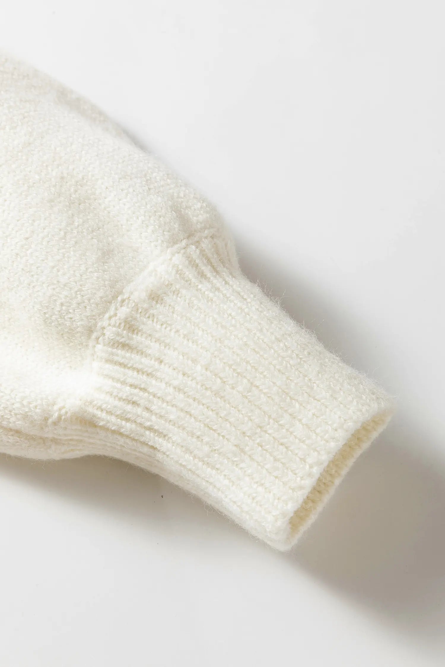 Close-up of a cream-colored knit garment sleeve with a ribbed cuff, shown on a clean white background.