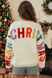 A woman viewed from behind wearing a cream-colored Christmas sweater with colorful fuzzy lettering that reads 'MERRY CHRISTMAS' on the back and sleeves, paired with green and white gingham shorts in a holiday decorated room.