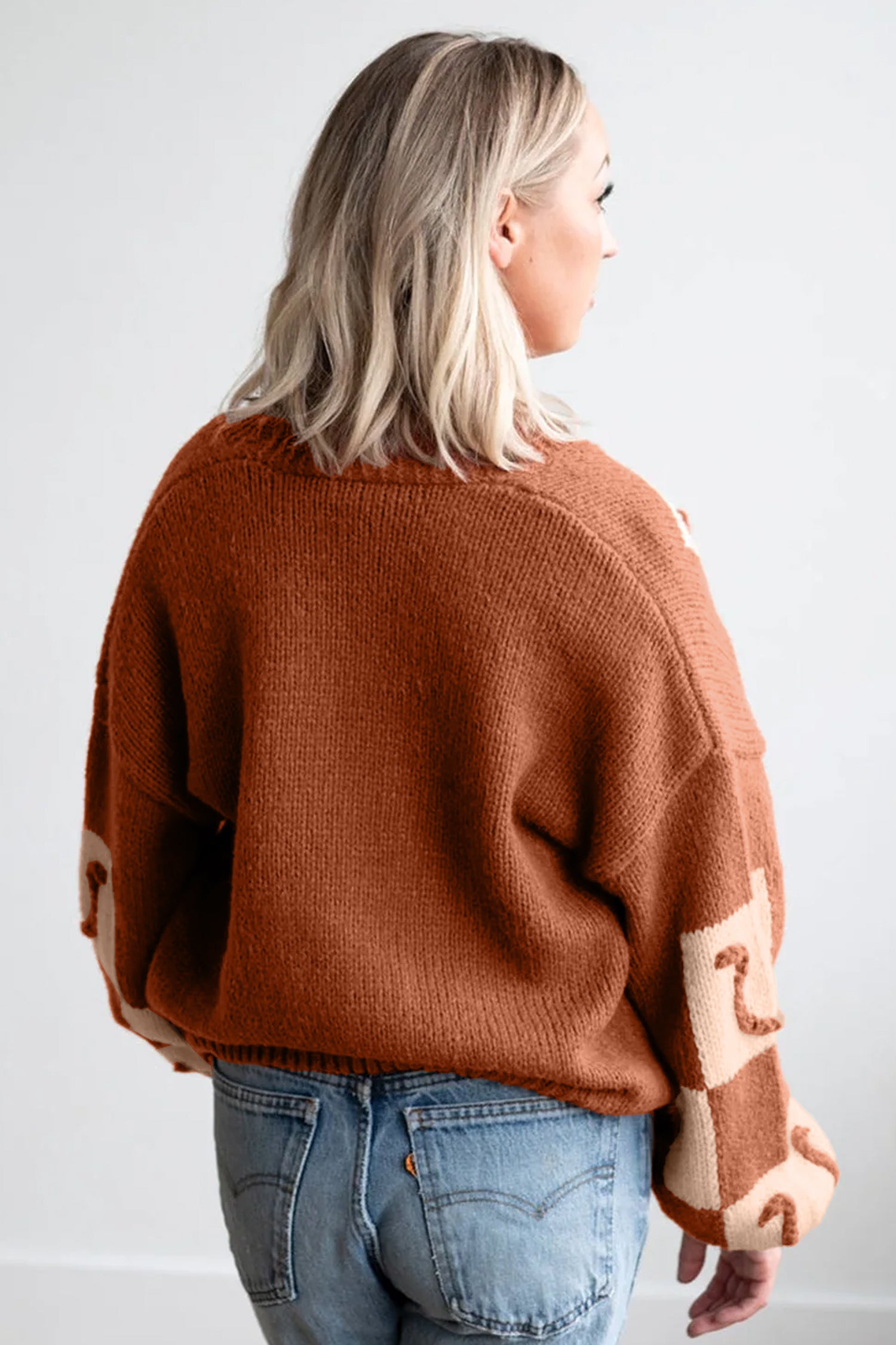 Back view of woman in rust-orange sweater with beige patchwork sleeves and blue jeans.