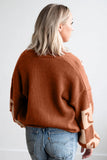 Back view of woman in rust-orange sweater with beige patchwork sleeves and blue jeans.