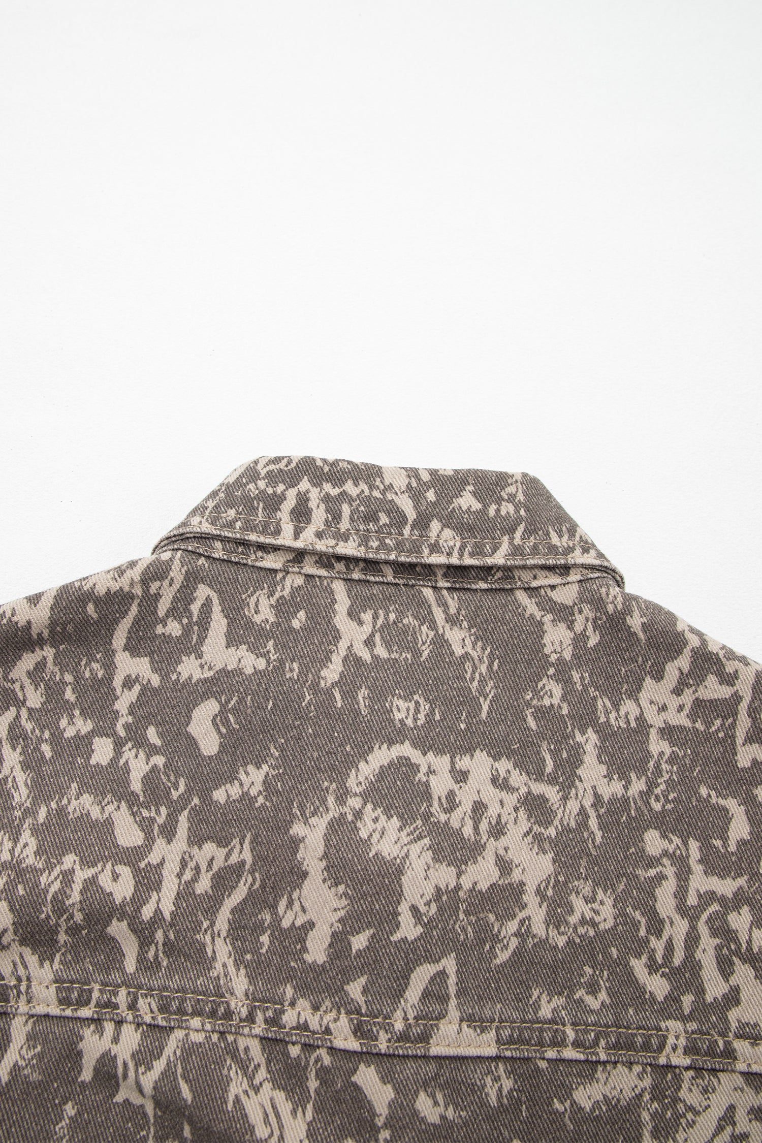 Close-up of the back collar and upper back of a canvas jacket in a distressed dark gray and beige mottled camouflage pattern.