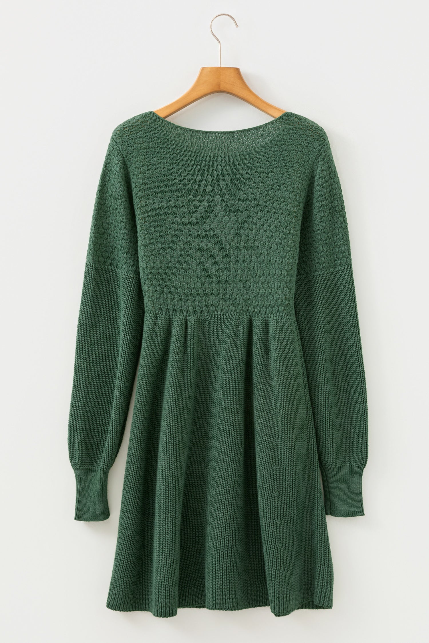 Green knitted dress on a wooden hanger against a white background
