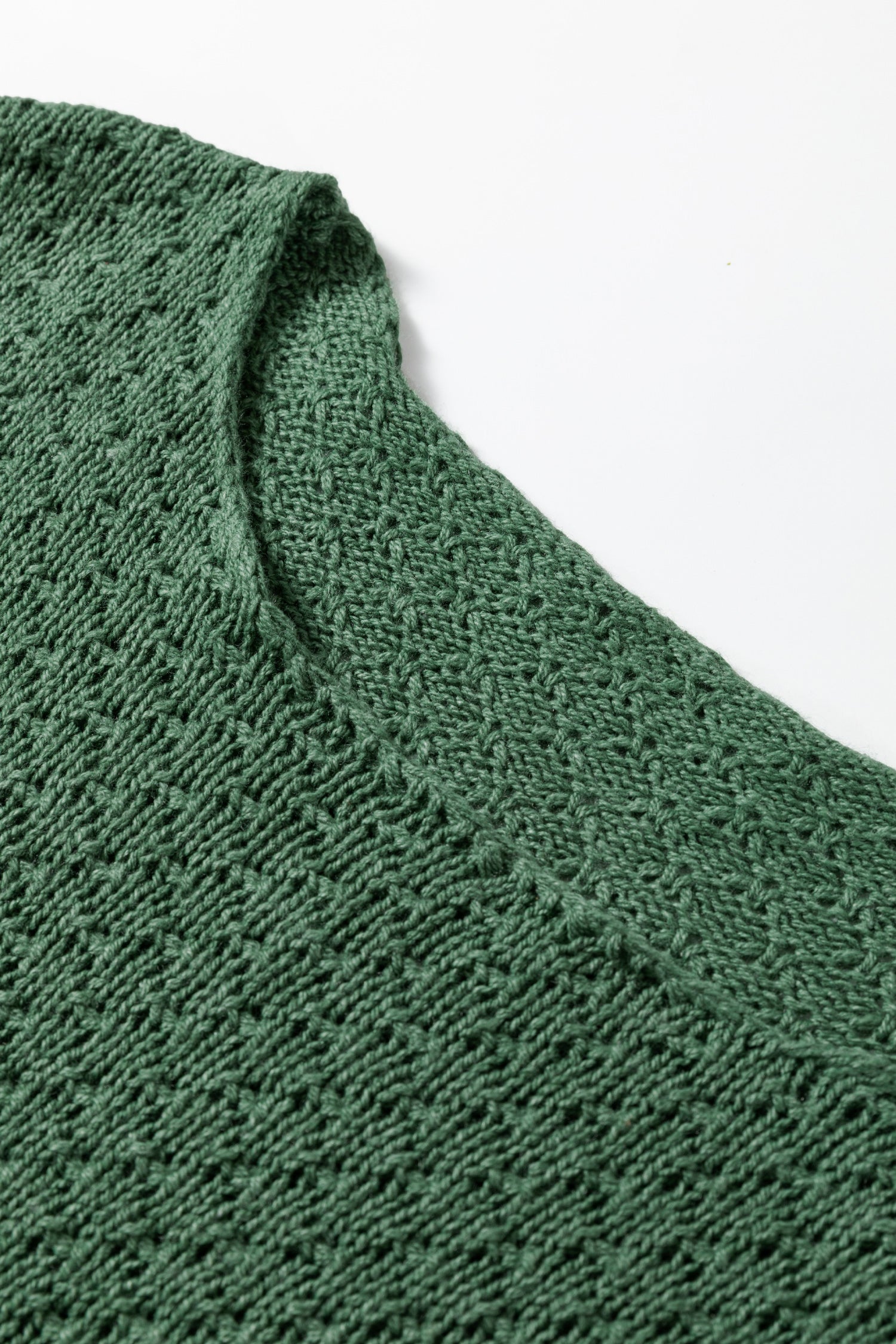 Close-up of a green knitted fabric with a textured pattern on a white background