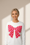 Woman wearing a white sweater with a pink heart bow design on a beige background
