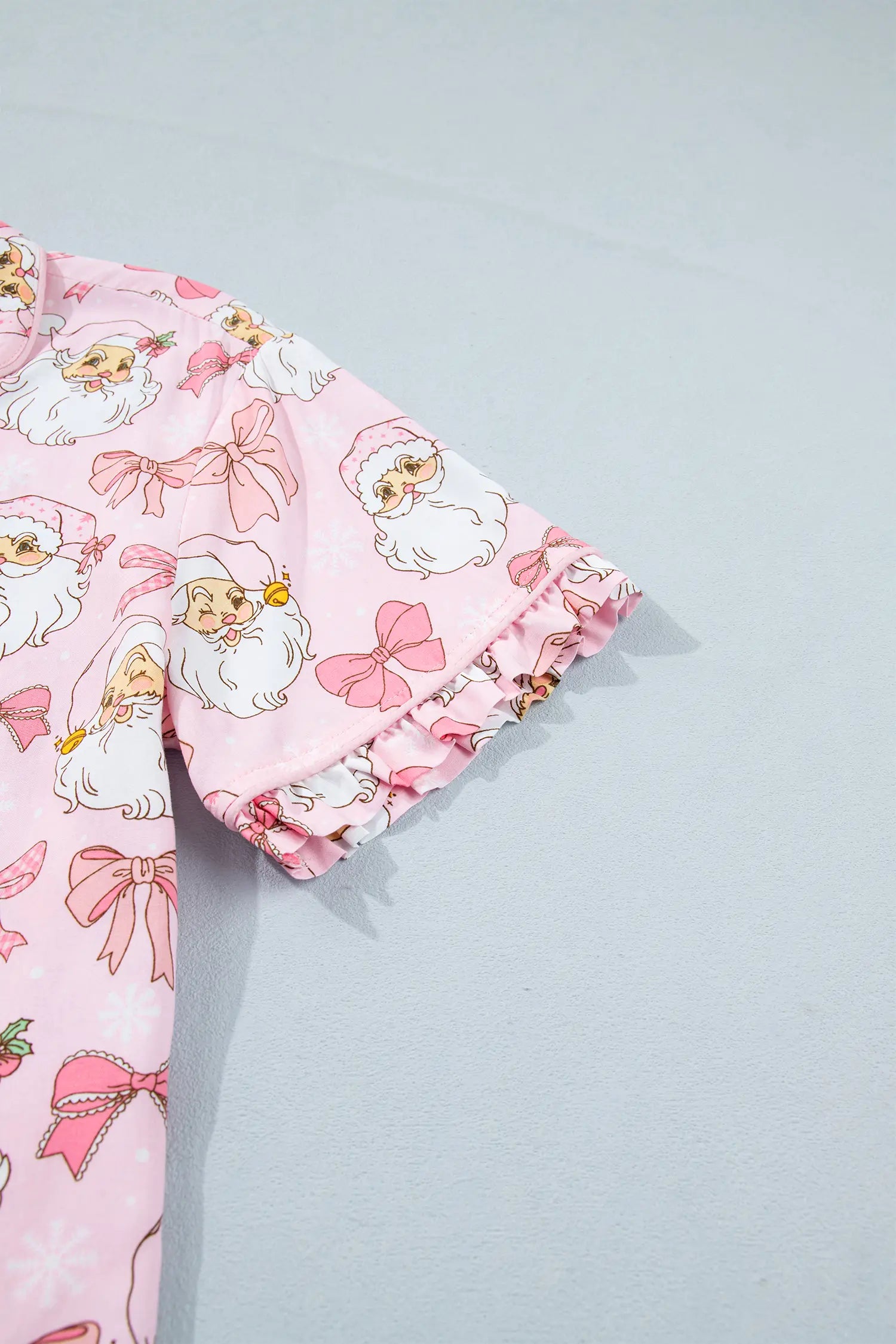 Close-up of pink pajama top with Santa and bow print and ruffled sleeve trim.