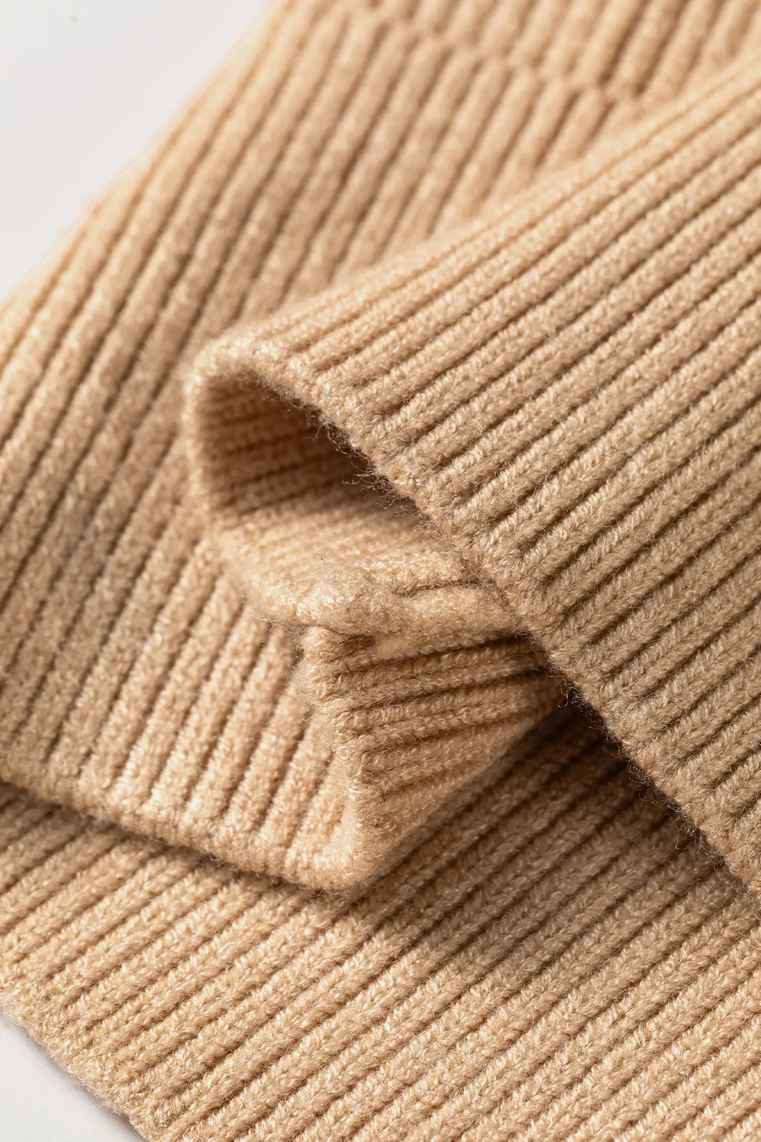 Close-up of a beige ribbed knit fabric, showing the soft texture and folded layers of the material.