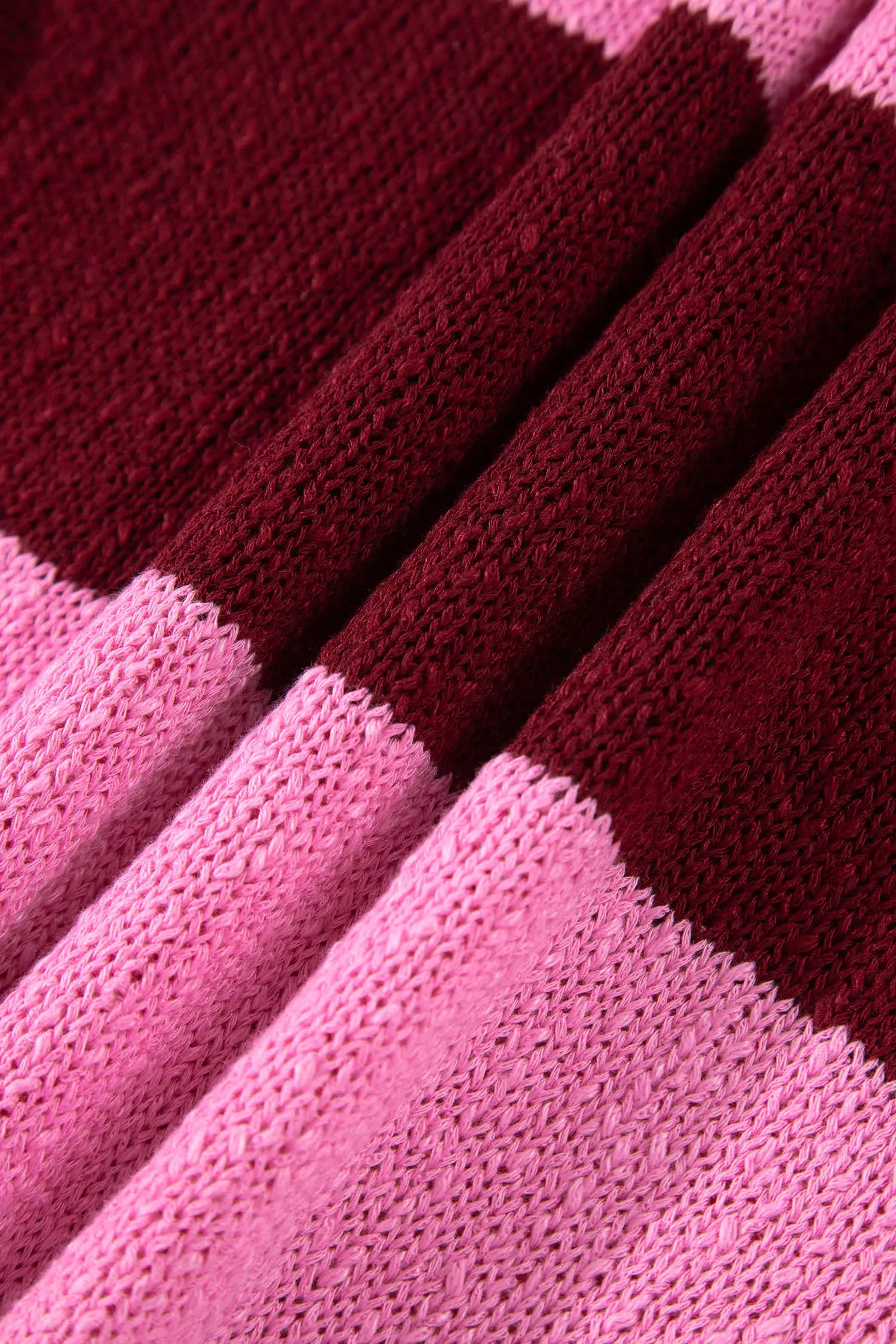 A close-up of folded knit fabric in alternating blocks of dark burgundy and light pink, showing the texture of the yarn.