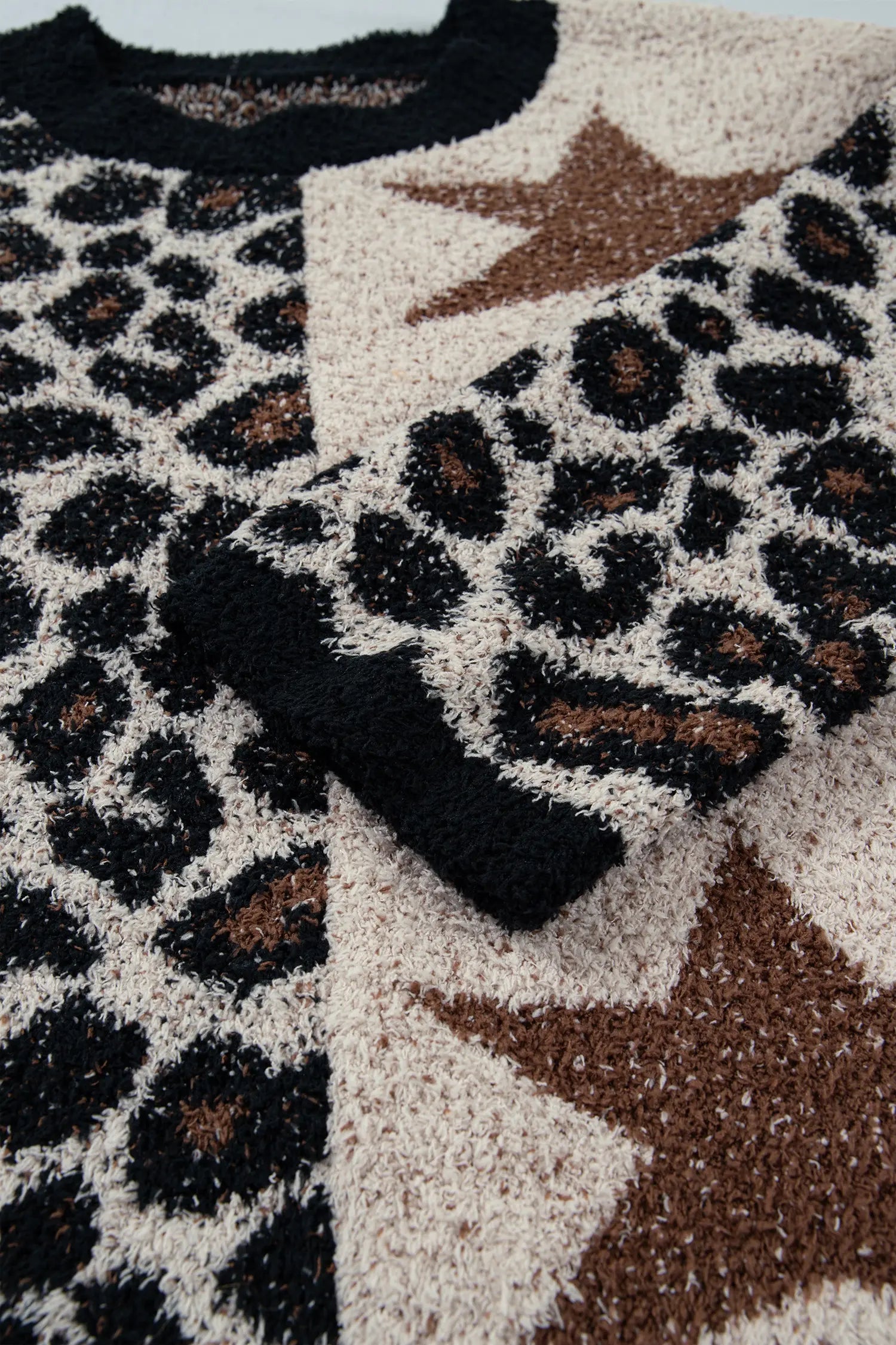 Close-up of a fuzzy knit sweater with a leopard print pattern in black and brown on a cream background, featuring large brown star motifs.