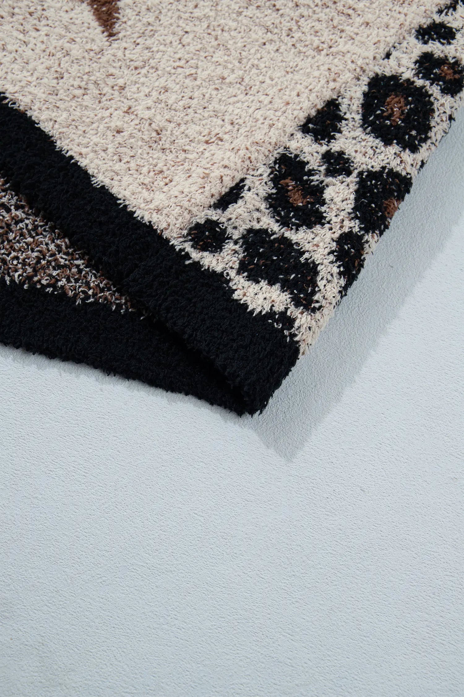 Close-up of a textured rug corner showing a beige and black leopard print pattern with a solid black border on a light gray background.