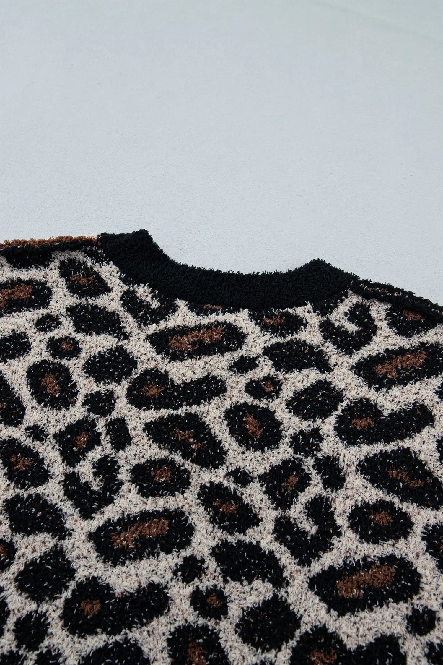 Close-up of a textured knit sweater featuring a leopard print pattern in black, brown, and cream, with a solid black ribbed crew neck.