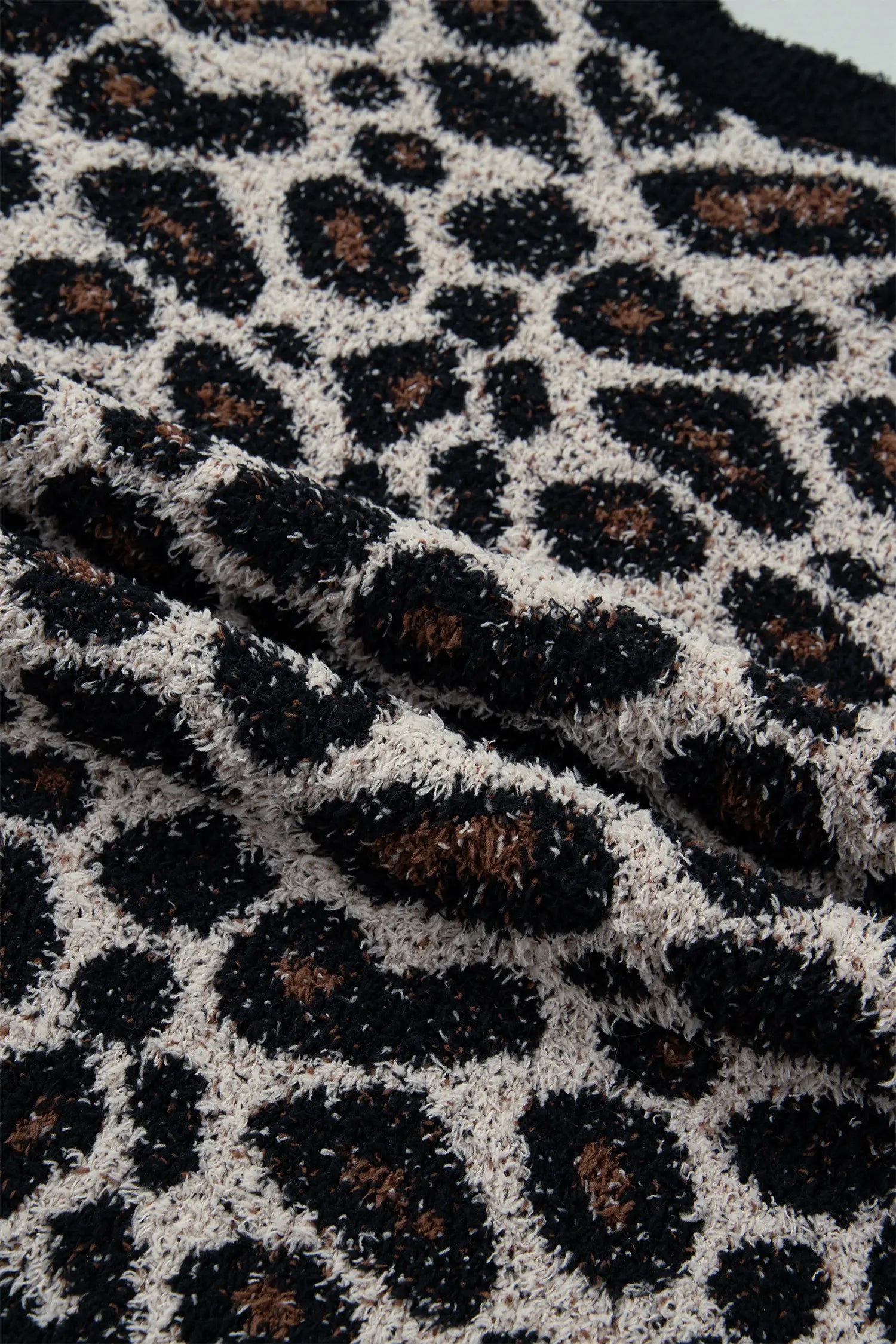 Close-up of a plush knit fabric with a leopard print pattern in black, beige, and brown.