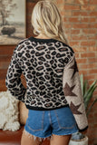 A woman viewed from behind wearing a fuzzy knit sweater with a leopard print on the back and a star pattern on one sleeve, paired with denim shorts in a rustic indoor setting.