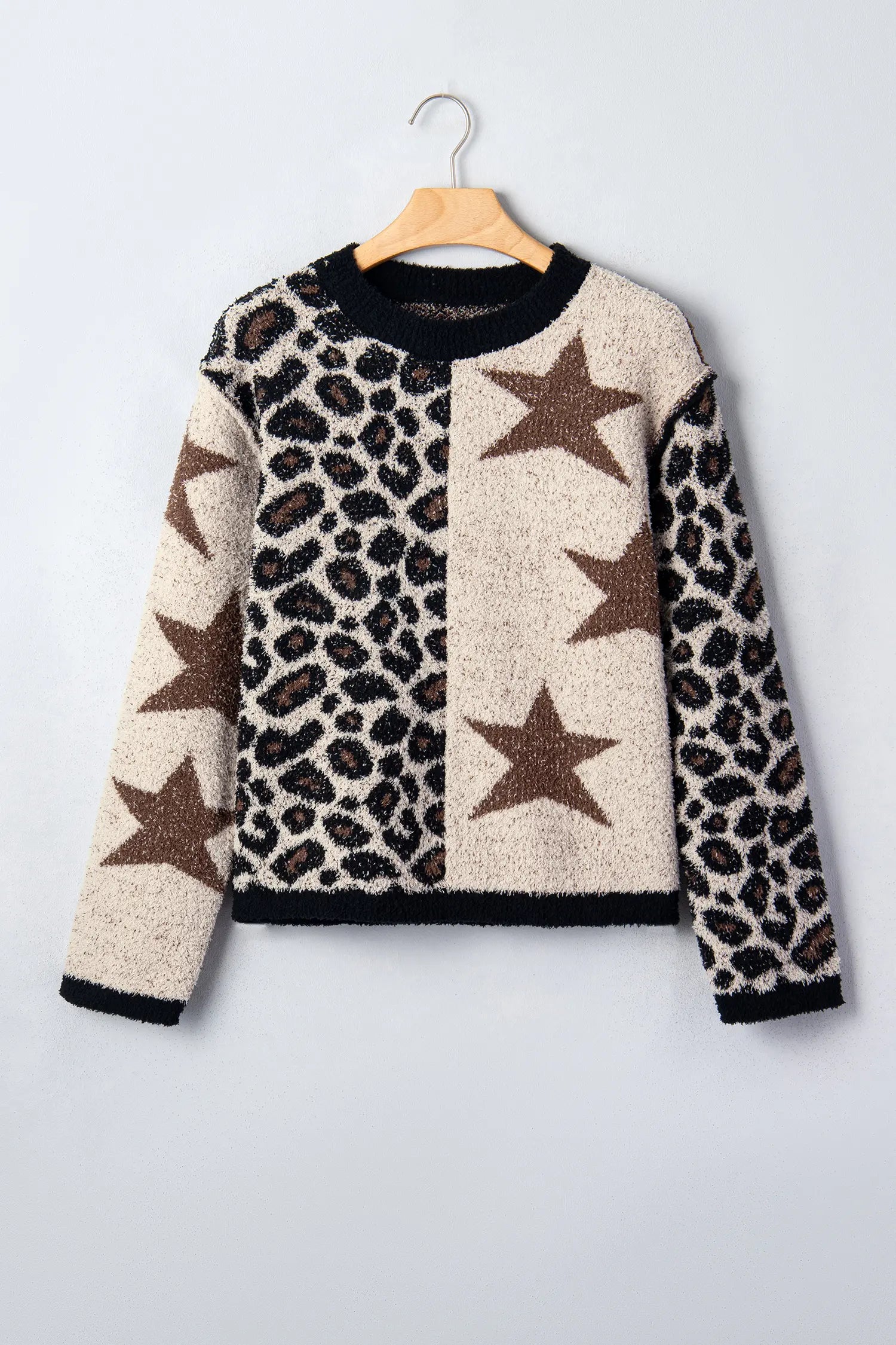 A fuzzy knit sweater with a leopard print and star pattern, hanging on a wooden hanger against a light gray background.