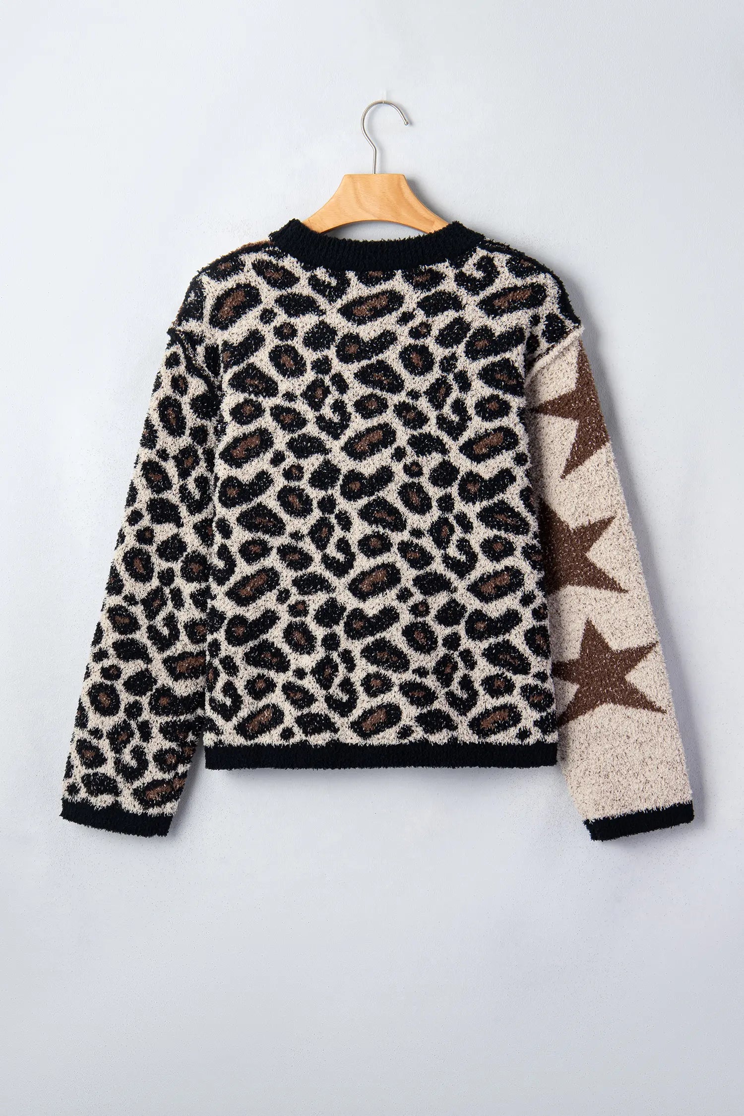 A fuzzy knit long-sleeve sweater with a leopard print pattern on the body and three large brown stars on one sleeve, hanging on a wooden hanger against a light gray background.
