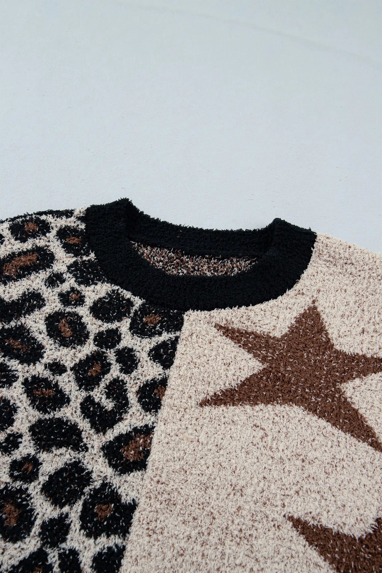 Close-up of a textured knit sweater with a split design: one side features a black leopard print on a beige background, and the other side features a large brown star on a beige background, with a solid black crew neck.