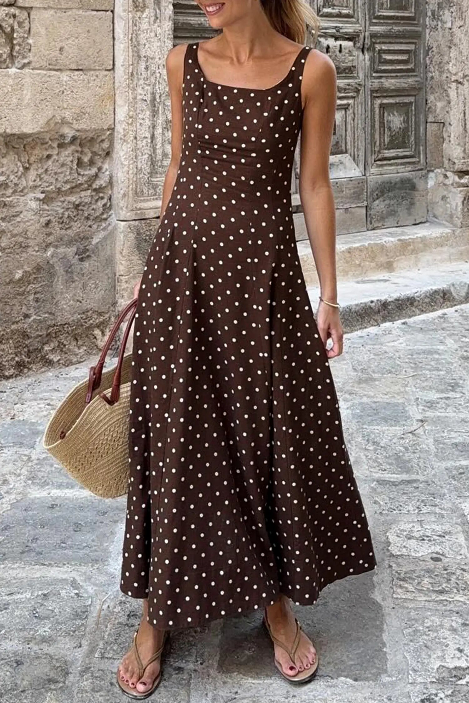 Woman wearing a brown polka dot dress standing on a stone street.