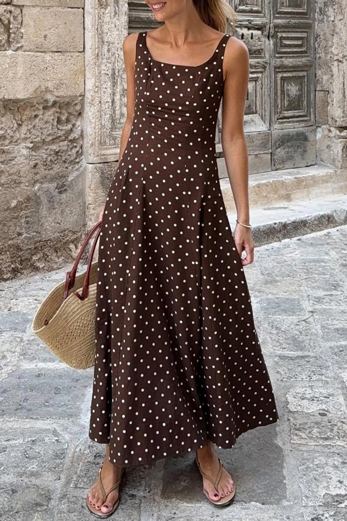 Woman wearing a brown polka dot dress standing on a stone street.