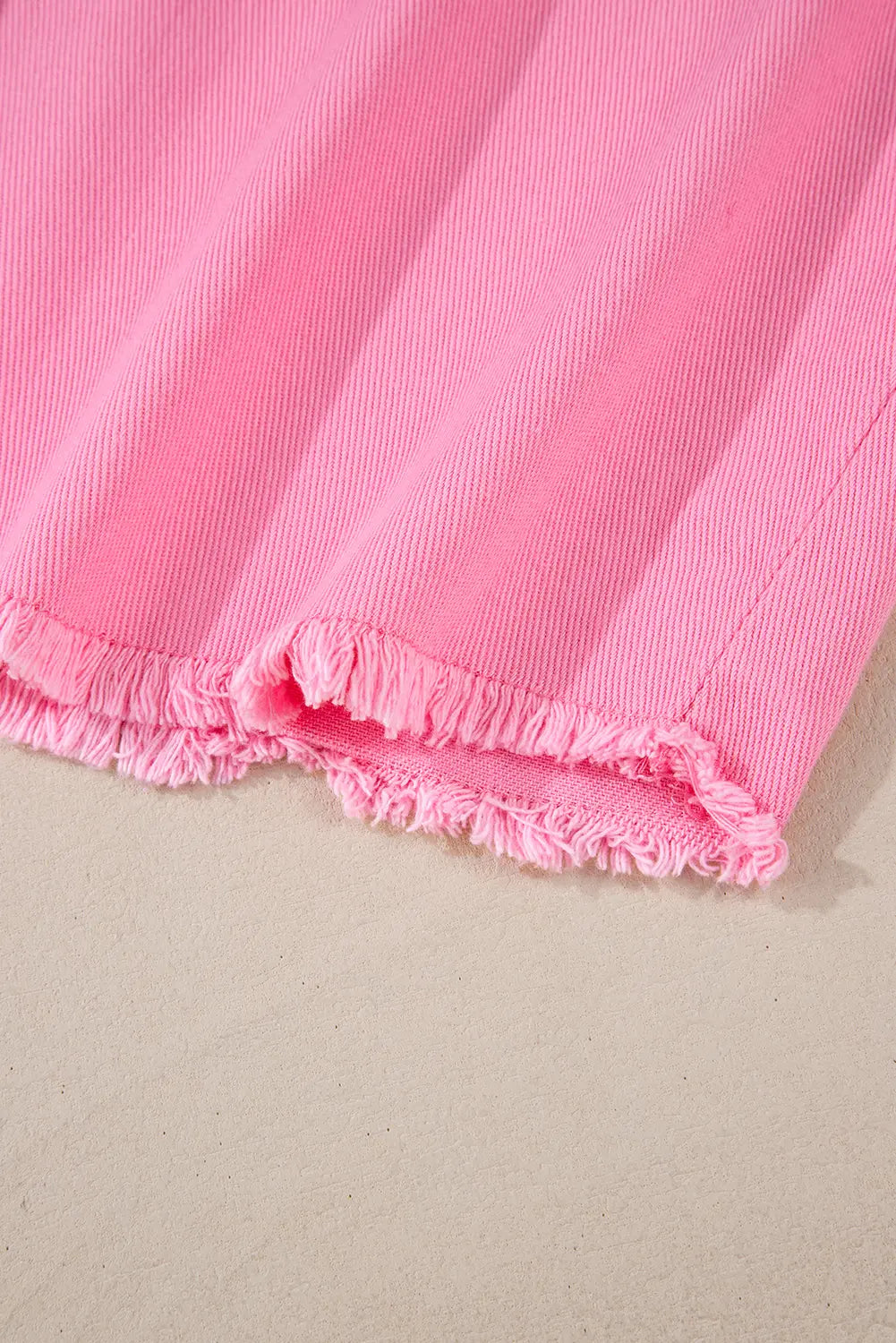 A close-up of bright pink frayed-edge fabric laid on a light beige surface.