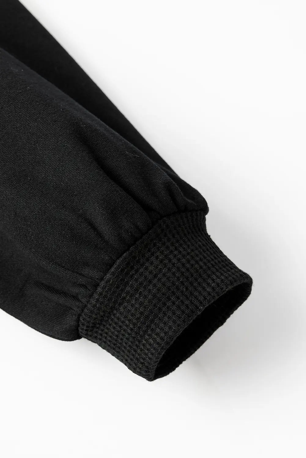 Close-up detail of a black sleeve with a ribbed elastic cuff on a white background.
