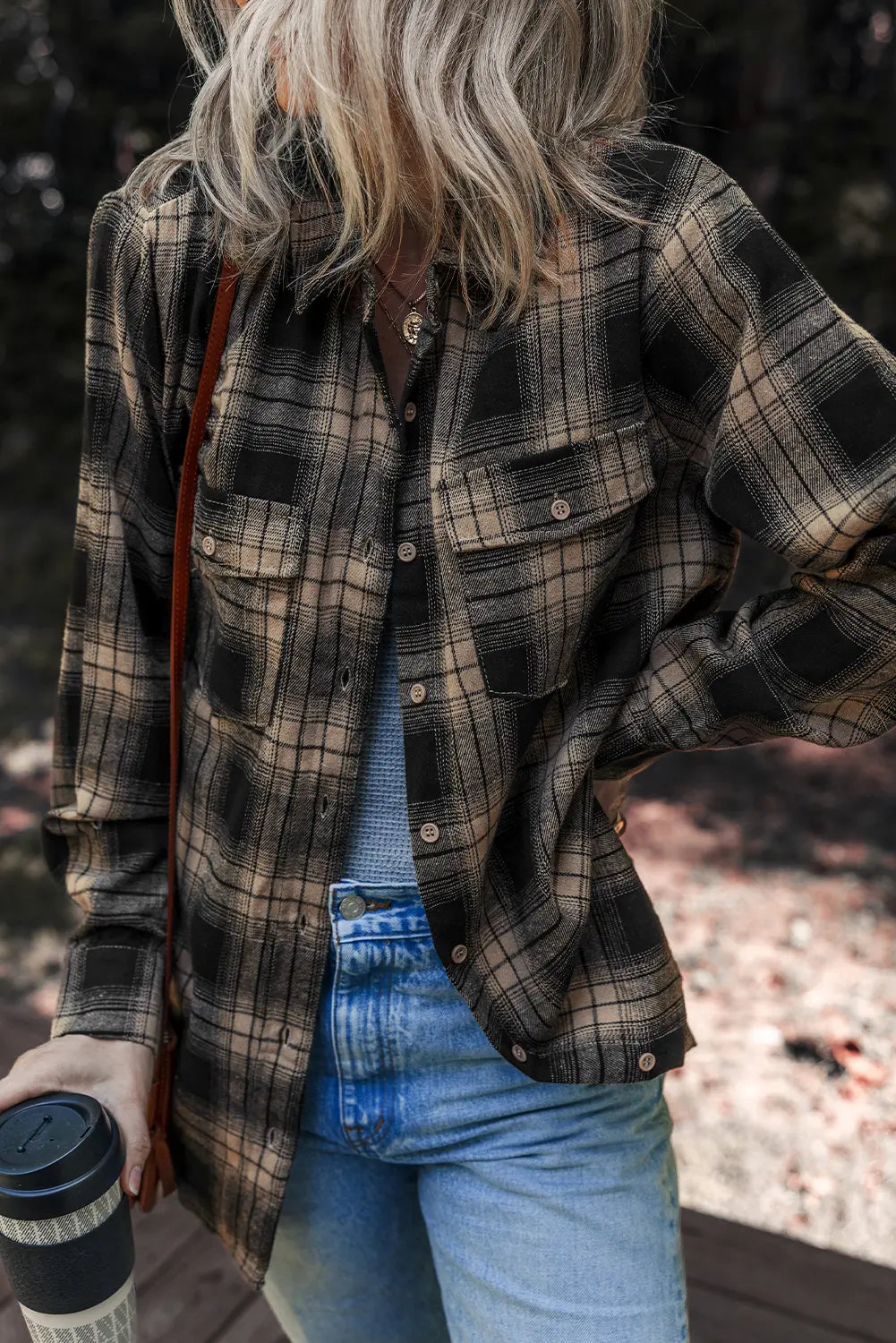 Person wearing a plaid shirt and jeans holding a coffee cup outdoors.