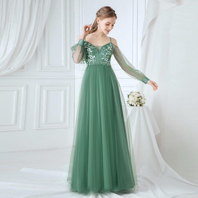 Woman wearing a green evening gown with floral lace details against a white curtain background