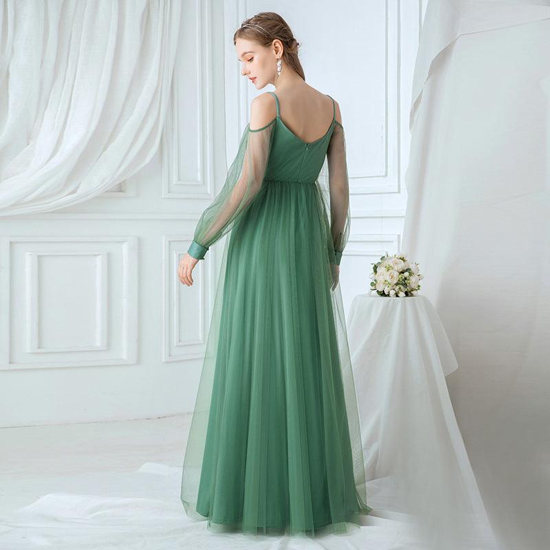 Woman in a green evening gown standing in a room with white curtains and a small table with flowers.