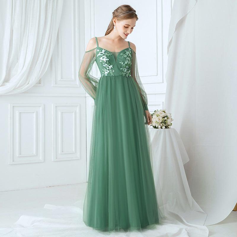 Woman in a green evening gown with floral lace top standing in a bright room.