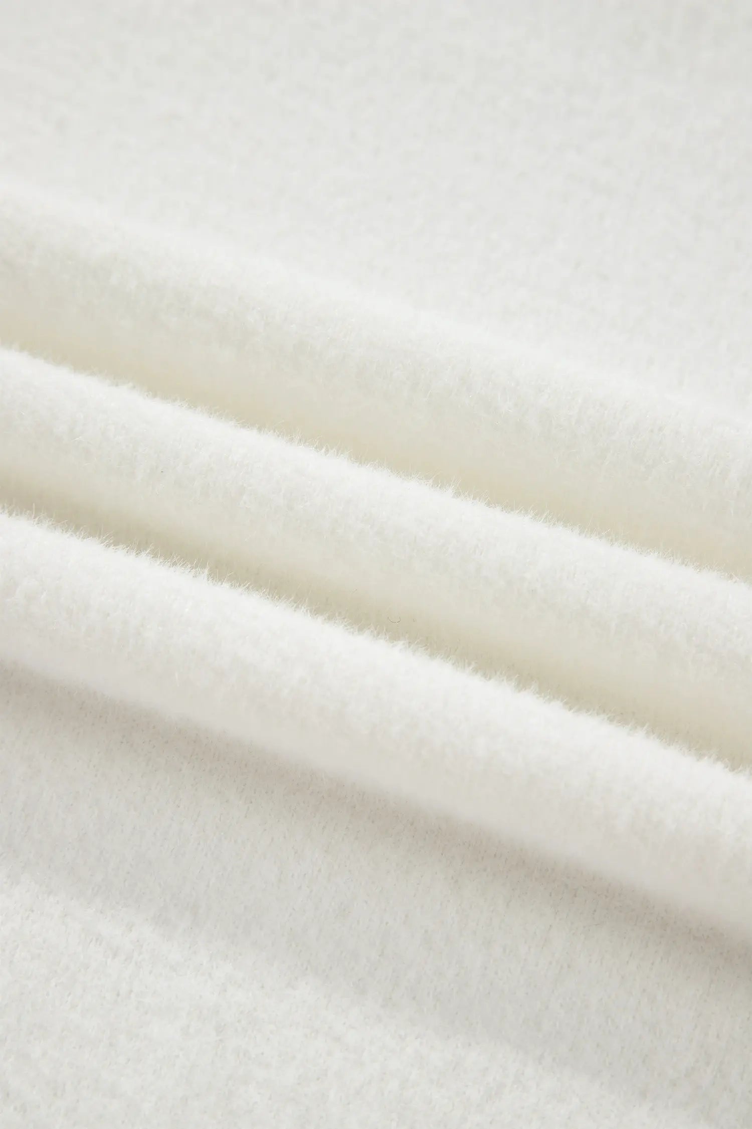 A close-up of soft, plush white fabric with gentle folds showing its textured surface.