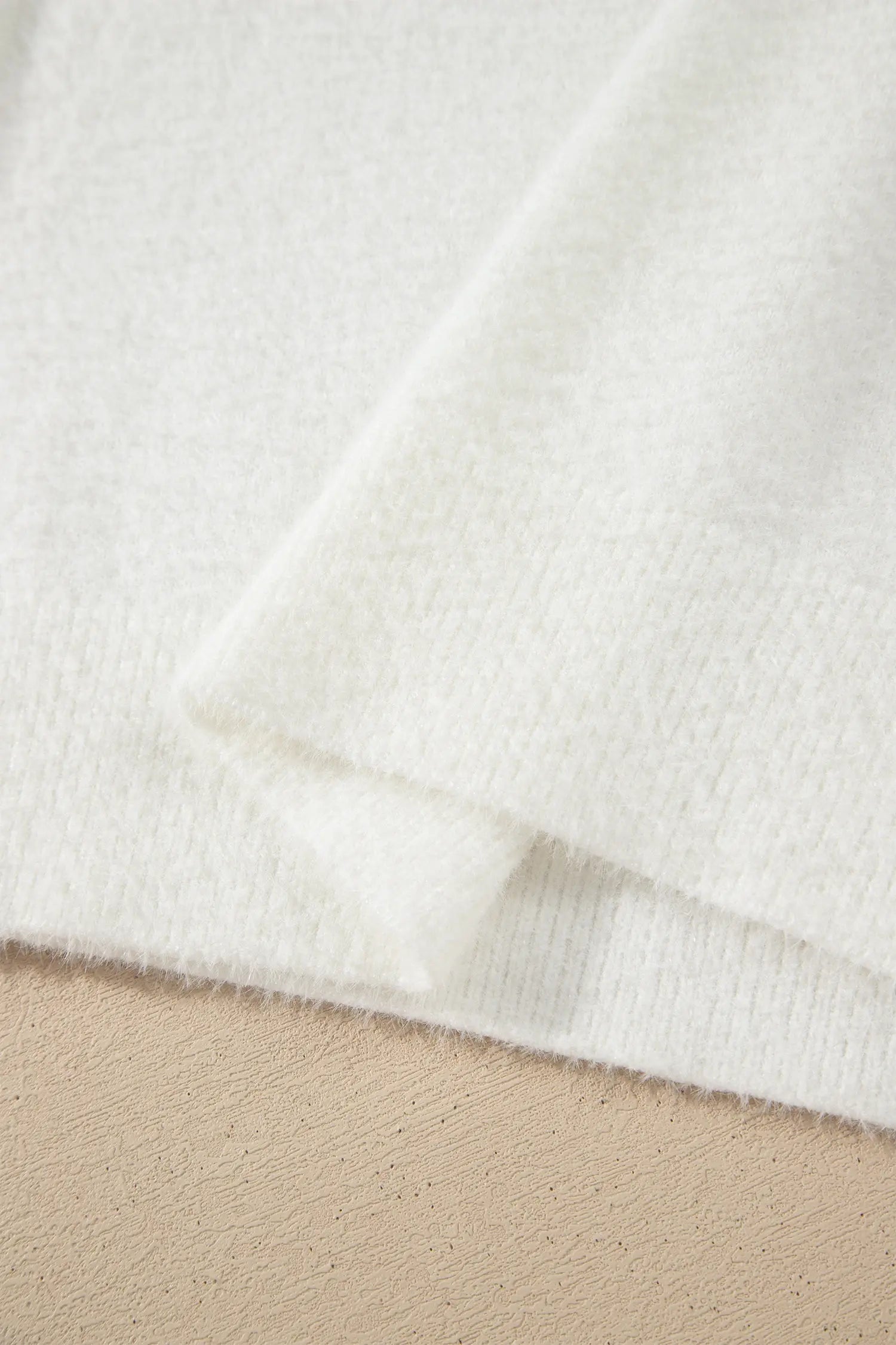 A close-up of soft, off-white knit fabric draped over a light beige textured surface.