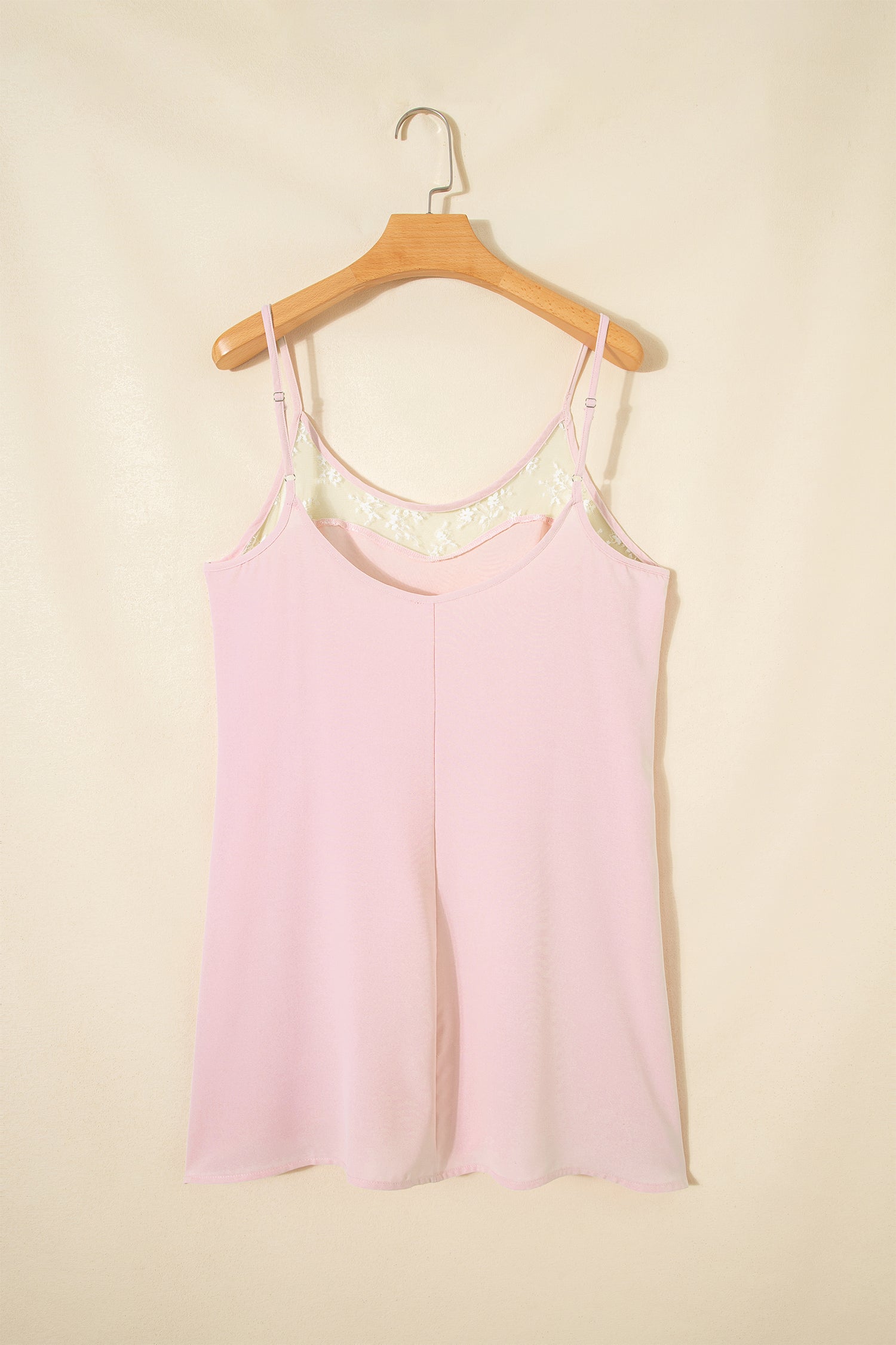 Pink tank top with lace trim on a wooden hanger against a beige background