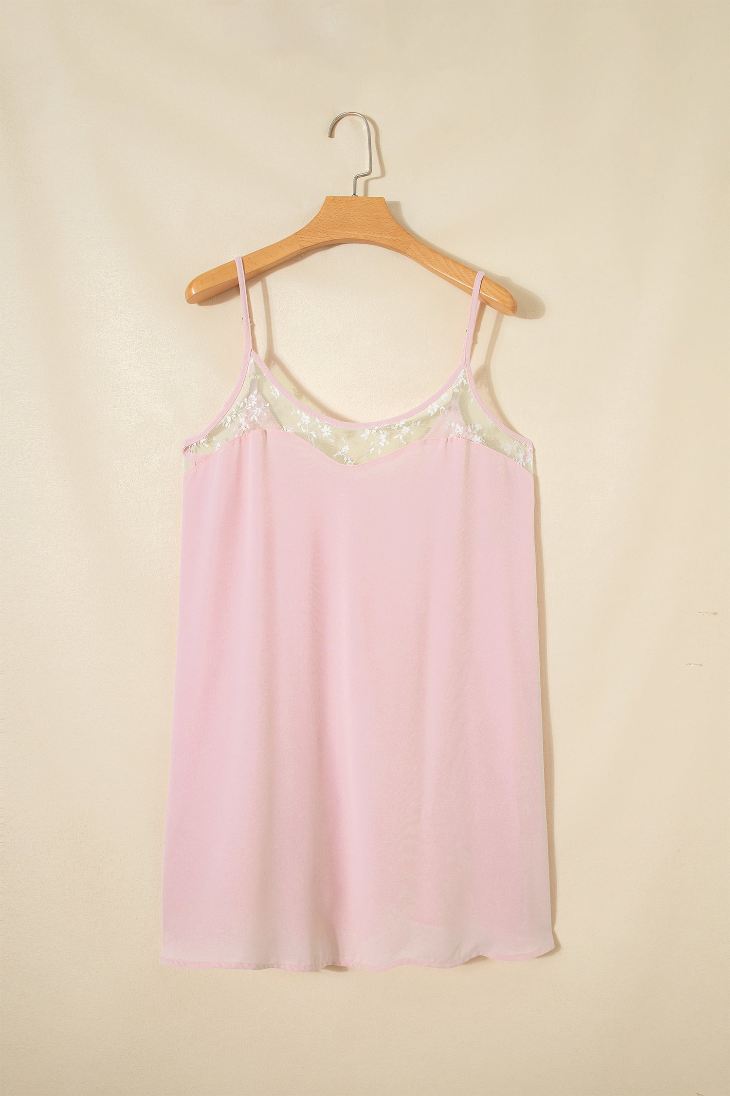 Pink slip dress with lace details on a wooden hanger against a beige background